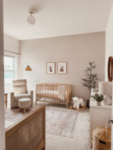 This gender neutral nursery features a crib, lamb rocker, olive tree, and bunny artwork.