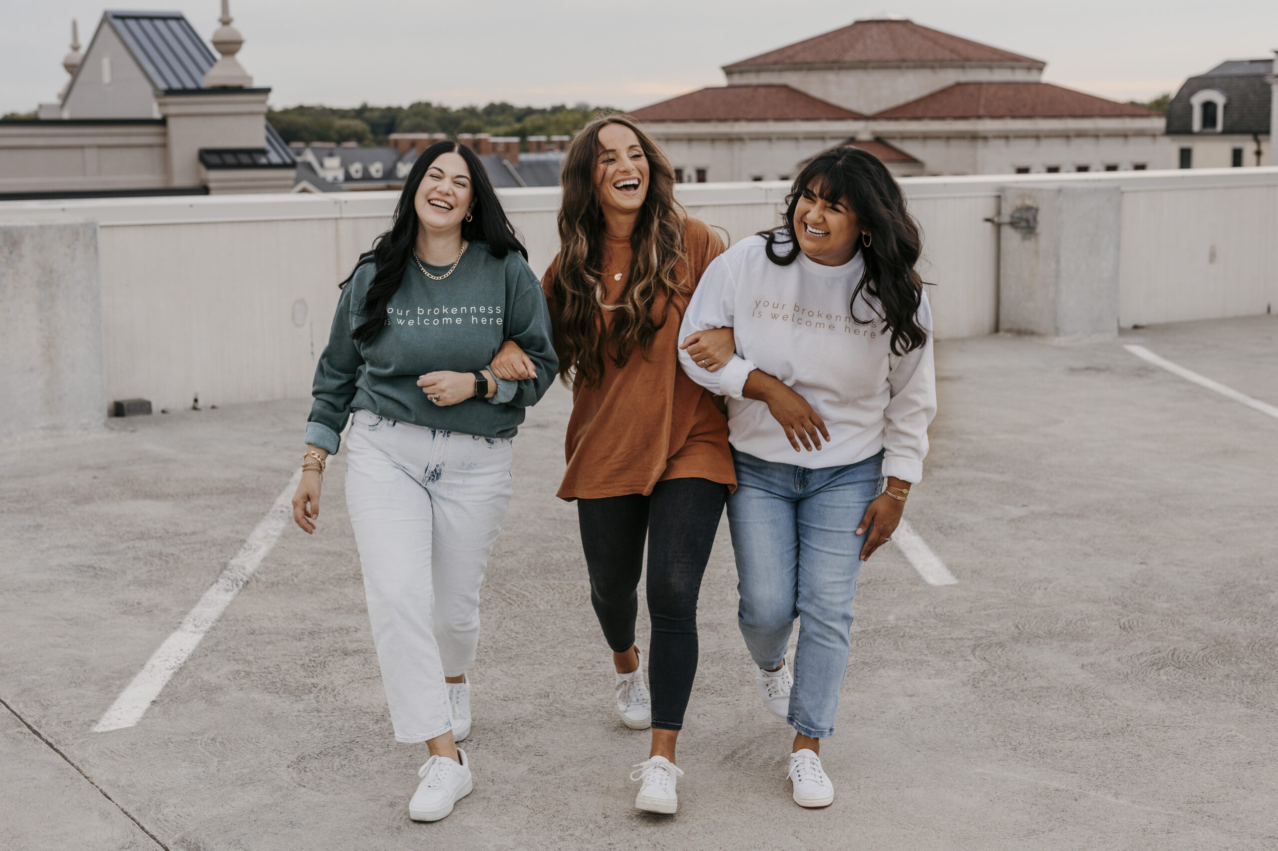 This image shows three friends walking and smiling with their arms linked.