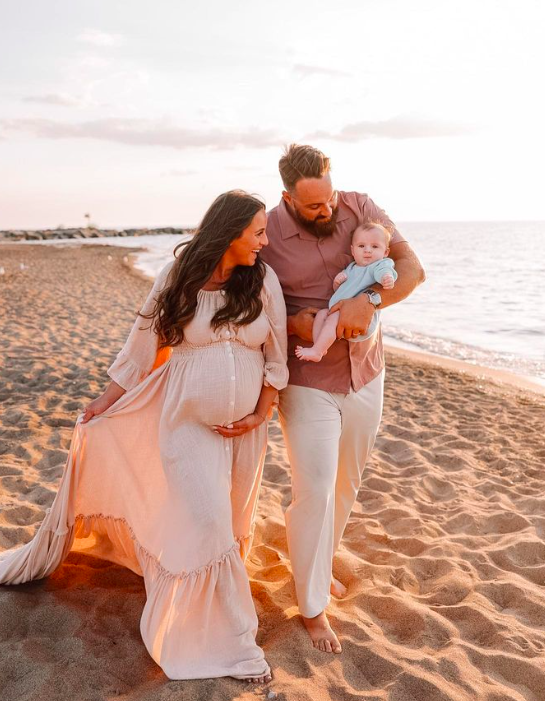 This image shows Jordan, pregnant, walking on the beach with her husband and son. Her family is navigating pregnancy after loss.