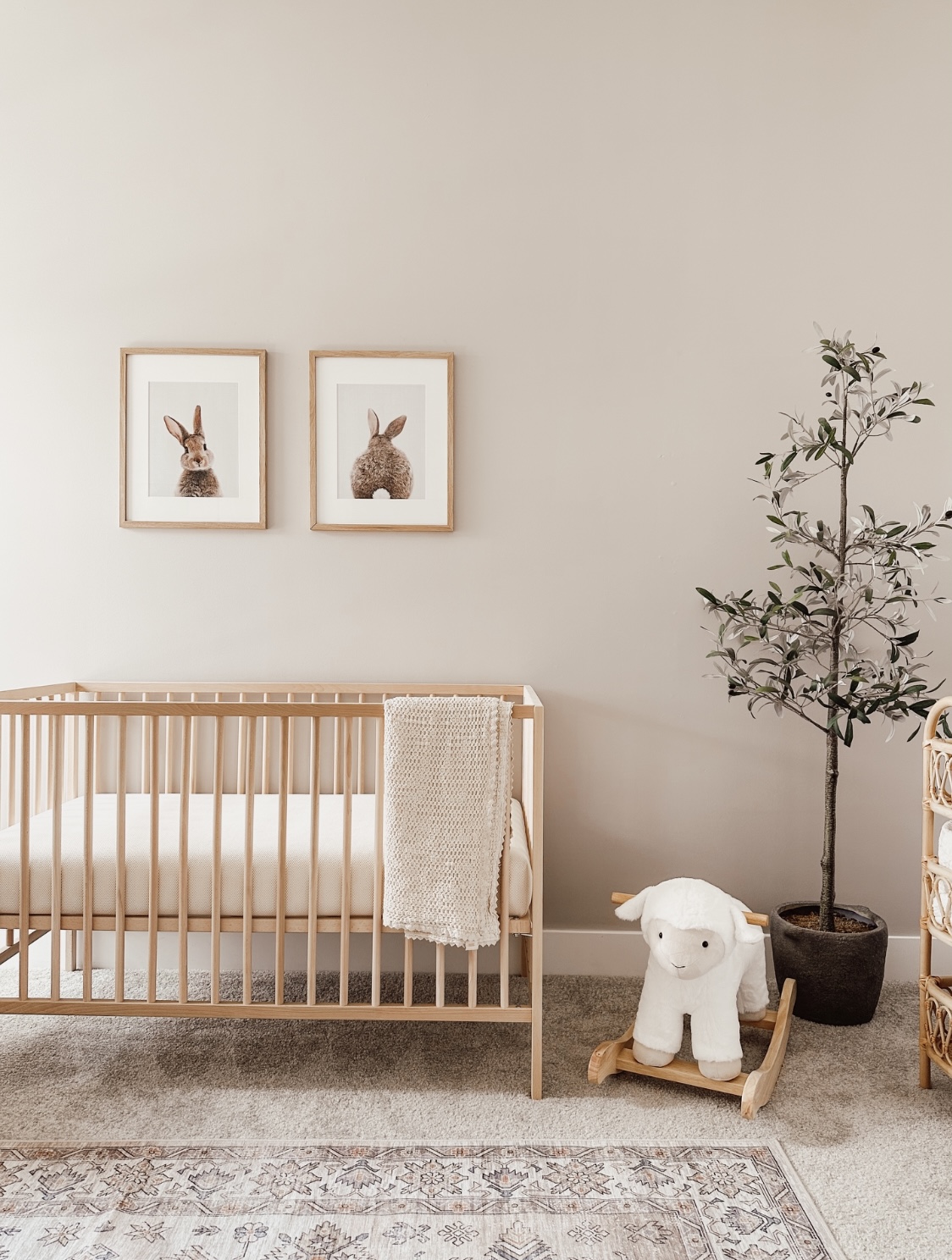 This nursery includes gender neutral walls, bunny artwork, a modern wooden crib, and a sheep rocker.