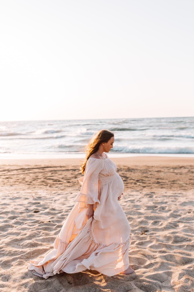 This image shows Jordan, pregnant, walking on the beach for her maternity photo. In this episode, she shares about her fertility journey and reproductive immunology.