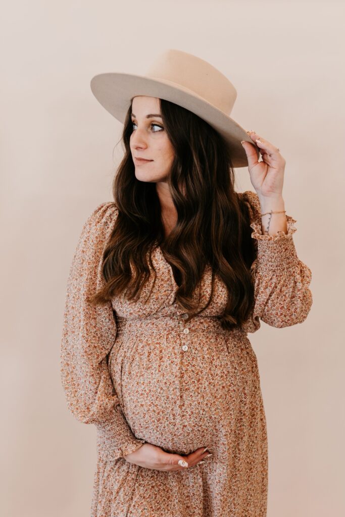 This is a maternity photo of Jordan. It shows her in a dress, with one hand on her belly and the other holding a hat. In this episode, she talks to Dr. Mae Hughes about pelvic floor health.