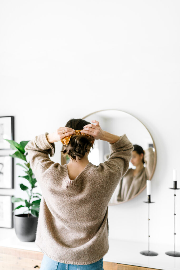 This image shows a woman looking in a mirror and putting her hair up. This episode explores the link between mental and hormonal health.