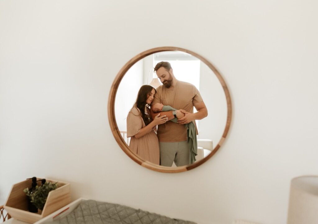 In this image, a mirror shows the reflection of Jordan and her husband holding their newborn son.